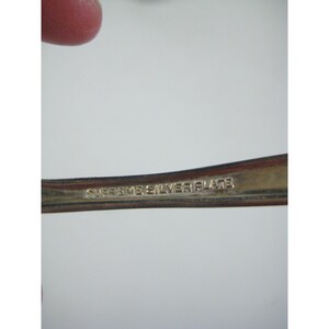 May include: Close-up of a silver-plated utensil with the text "SUPREME SILVER PLATE" engraved on the handle. The utensil has a shiny, reflective surface, and the text is in a serif font.