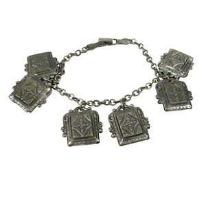 May include: A silver-toned charm bracelet featuring five rectangular pendants. Each pendant displays an embossed floral pattern with a central cross-like motif and decorative borders. The bracelet is constructed with a simple link chain and a clasp.