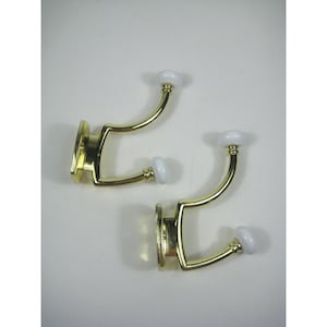 May include: Two gold-toned wall hooks with white ceramic finials. Each hook has a double-prong design.