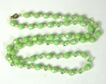 May include: A delicate necklace featuring faceted, light green beads. The necklace has a gold-tone clasp and is interspersed with smaller, lighter green and yellow beads. The beads are strung together, creating a graceful, flowing design.