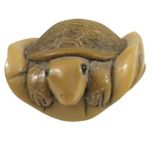 May include: A detailed, tan-colored turtle figurine. The turtle's shell has a textured pattern, and its head and limbs are visible. The figurine is likely made of a hard material, and the overall design is intricate and detailed.