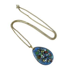 Puede incluir: Un collar vintage dorado con un colgante. El colgante tiene un fondo de esmalte azul con acentos moteados de colores en verde, rojo, amarillo y blanco. La cadena del collar es delicada y de color dorado.