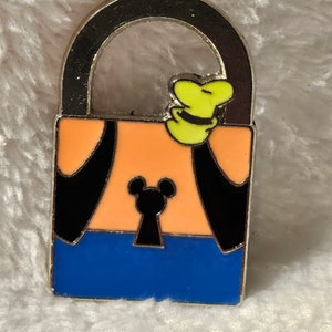 May include: A silver metal padlock with a blue, orange, and black design. The padlock has a Mickey Mouse head on the front and a small yellow figure on top.