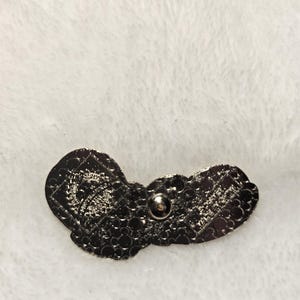 Puede incluir: Un pin de metal gris oscuro con un dise&ntilde;o de mariposa. El pin tiene una superficie texturizada y un respaldo de alfiler para la fijaci&oacute;n. El dise&ntilde;o de la mariposa es detallado e intrincado, con patrones visibles en las alas.