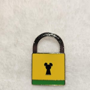 May include: A yellow padlock with a silver handle and a black keyhole shaped like a mouse. The bottom of the lock has a green stripe. The lock is a decorative item.