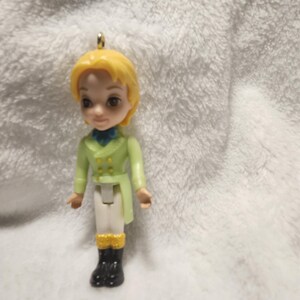 Peut inclure: Petite figurine en plastique représentant un jeune homme aux cheveux blonds, vêtu d'un manteau vert clair, d'un pantalon blanc et de bottes noires. La figurine a une boucle dorée en haut pour l'accrocher. Objet de collection.