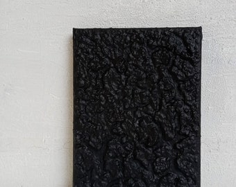 Könnte beinhalten: Ein schwarzes Leinwandbild mit einer strukturierten Oberfläche. Die Struktur erinnert an eine felsige oder bergige Landschaft.