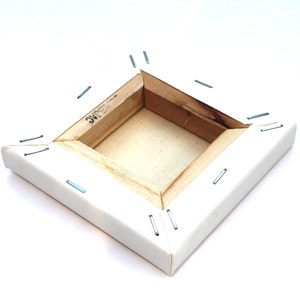 May include: A white canvas stretched over a wooden frame with staples securing the canvas to the frame. The back of the canvas is visible, showing the wooden frame and staples.