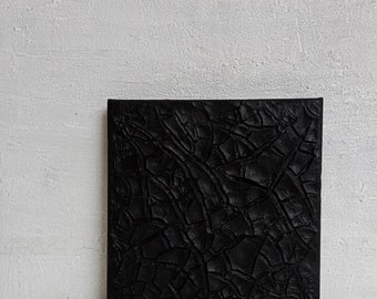 Könnte beinhalten: Schwarzes quadratisches Leinwandbild mit einer strukturierten, rissigen Oberfläche. Die Textur ähnelt rissiger Erde oder getrocknetem Schlamm.