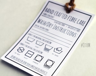 May include: A white tag with black text and symbols for hand-crafted fiber care instructions. The tag is tied with a brown twine string. The text reads "HAND CRAFTED FIBRE CARE" and "WASH/DRY INSTRUCTIONS:" with symbols for washing, drying, and ironing. The tag also includes the hashtag #OTHM.