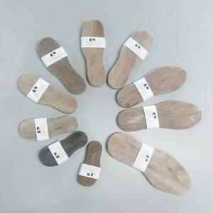 May include: A collection of 10 wooden insoles with a white label that says "Alpaca" and "Alpacadirect.com". The insoles are arranged in a circle on a light gray surface.
