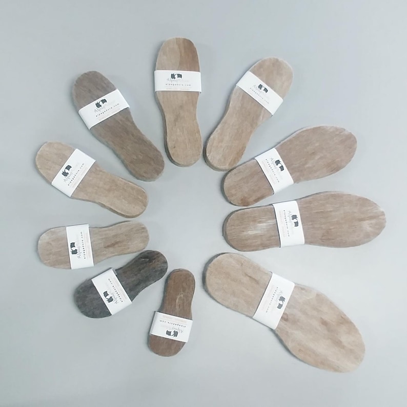 May include: A collection of 10 wooden insoles with a white label that says "Alpaca" and "Alpacadirect.com". The insoles are arranged in a circle on a light gray surface.