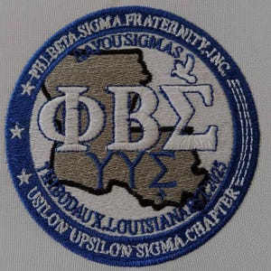 Può includere: Una toppa ricamata circolare con il logo della confraternita Phi Beta Sigma, Inc. con lettere greche bianche, una mappa beige della Louisiana e il testo blu Thibodaux Louisiana Upsilon Upsilon Sigma Chapter su sfondo bianco.