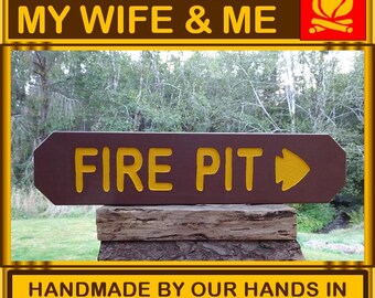 May include: A brown wooden sign with yellow lettering that reads "FIRE PIT" with a yellow arrow pointing to the right. The sign is handmade and says "HAND CRAFTED BY MY WIFE & ME" and "HANDMADE BY OUR HANDS IN SOLITUDE VALLEY OREGON".