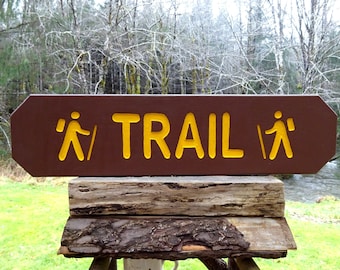 May include: A brown wooden sign with yellow text and hiker symbols reads "TRAIL".