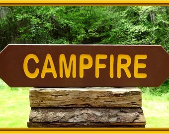 May include: A brown wooden sign with the word "CAMPFIRE" in yellow letters. The sign is mounted on a stack of weathered logs.