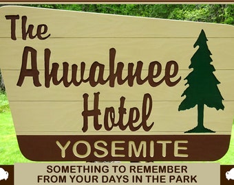 May include: Wooden sign for The Ahwahnee Hotel in Yosemite. The sign features the hotel name and "YOSEMITE" in a brown font on a light beige background. A green tree silhouette is on the right. The bottom reads "SOMETHING TO REMEMBER FROM YOUR DAYS IN THE PARK."