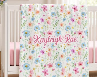 May include: A white baby blanket featuring a repeating watercolor floral pattern in shades of pink, blue, and yellow with green foliage. The name Kayleigh Rae is printed in a pink cursive script across the center of the blanket.