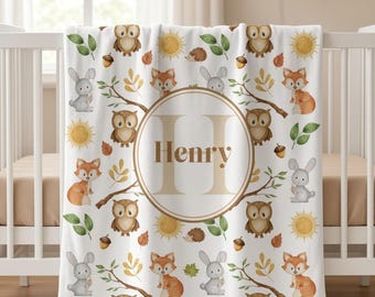 May include: A white baby blanket featuring a repeating pattern of watercolor owls, foxes, rabbits, hedgehogs, acorns, leaves, and suns. In the center, a large circular frame contains a capital letter H and the name Henry in brown text.