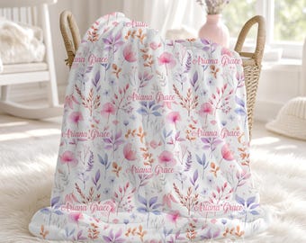 May include: A white throw blanket featuring a repeating watercolor botanical pattern in shades of pink, purple, and orange. The name Ariana Grace is printed in a cursive script throughout the fabric, interspersed among the floral illustrations.
