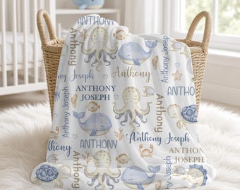 May include: A white baby blanket featuring a repeating pattern of blue and beige sea creatures including octopuses, whales, turtles, crabs, and fish, interspersed with the printed names Anthony and Anthony Joseph in various blue and brown fonts.