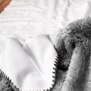 A close-up view of a soft, fluffy gray blanket with a white, crumpled texture, resting on a white surface.