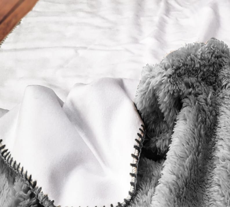 A close-up view of a soft, fluffy gray blanket with a white, crumpled texture, resting on a white surface.