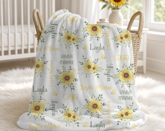 May include: A white fleece blanket featuring a repeating pattern of yellow sunflowers, green leaves, and small yellow butterflies. The text Layla and Layla Maree is printed in various fonts and colors, including yellow and dark gray, across the fabric.