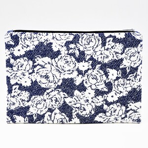 Puede incluir: Una bolsa de cremallera azul y blanca con estampado floral. La bolsa está hecha de una tela texturizada con un estampado floral blanco sobre un fondo azul oscuro.