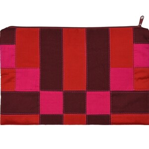 Könnte beinhalten: Eine rote, rosafarbene und braune Patchwork-Kosmetiktasche mit Reißverschluss. Die Tasche ist aus Stoff und hat ein geometrisches Muster.