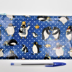 May include: A blue zippered pouch with a white background and a pattern of penguins wearing hats and holding various objects. The pouch is decorated with white polka dots.