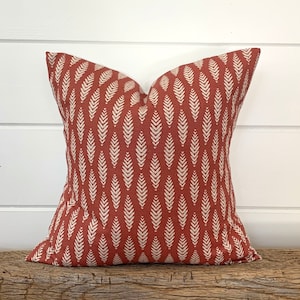 May include: A rust-colored throw pillow with a white leaf pattern. The pillow is made of a soft, textured fabric.