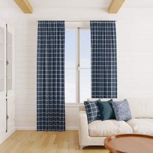 May include: Navy blue and white checkered curtains hanging in front of a window. The curtains are paired with a white sofa and decorative pillows. The room has white walls and a wooden coffee table.