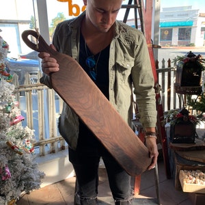 May include: A person holding a large, dark brown wooden serving board with a unique handle. The board has a natural wood grain pattern and appears to be handmade.