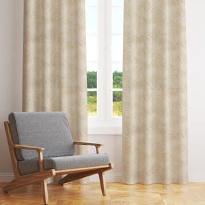 May include: Beige curtains with a subtle palm leaf pattern hang in front of a window with a view of green trees. A grey armchair with wooden legs sits in front of the curtains.