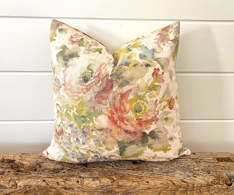 May include: A decorative pillow with a floral pattern in shades of pink, green, and beige. The pillow is made of linen and has a subtle watercolor effect.