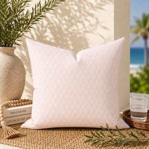 May include: A square throw pillow in a soft pastel pink color featuring a repeating white leaf or teardrop pattern. The pillow has a smooth, uniform texture and is filled to create a plump, structured shape with crisp, clean edges.