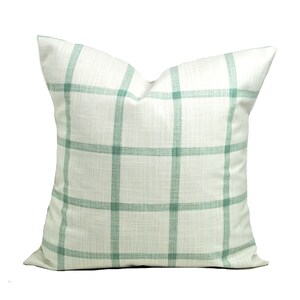 Pu&ograve; includere: Cuscino decorativo quadrato con sfondo bianco e motivo a griglia in un delicato verde. Il cuscino ha un aspetto strutturato ed &egrave; probabilmente in tessuto. Un elemento di arredo per la casa.
