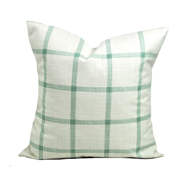 Pu&ograve; includere: Cuscino decorativo quadrato con sfondo bianco e motivo a griglia in un delicato verde. Il cuscino ha un aspetto strutturato ed &egrave; probabilmente in tessuto. Un elemento di arredo per la casa.