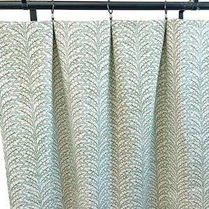 May include: Curtains with a repeating leaf pattern in shades of green and white. The fabric is hanging from a black rod with metal rings. The curtains have a soft, flowing appearance.