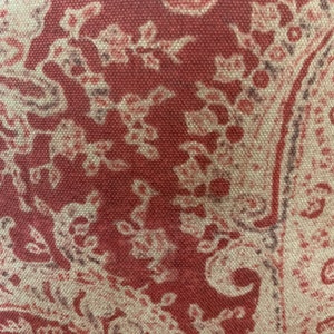 May include: Close-up of a red fabric with a white paisley pattern. The fabric has a textured surface and a subtle sheen.