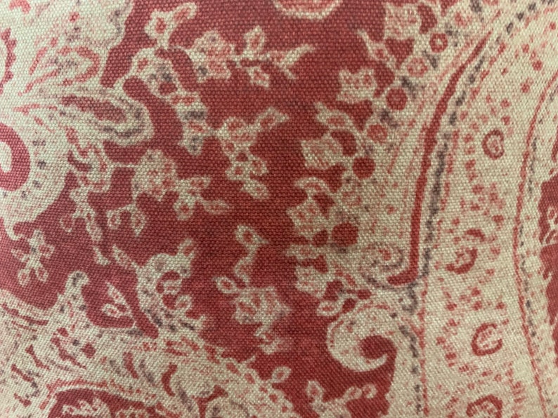May include: Close-up of a red fabric with a white paisley pattern. The fabric has a textured surface and a subtle sheen.