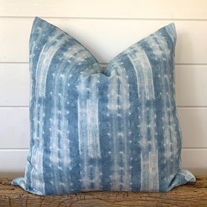 May include: A blue and white patterned throw pillow with a subtle tie-dye effect. The pillow is made of a soft, textured fabric and has a square shape.