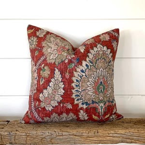 May include: Red and cream patterned throw pillow with a floral design. The pillow is made of a soft, textured fabric.