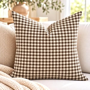 May include: A square throw cushion featuring a classic brown and white gingham check pattern. The fabric displays a consistent grid of small, alternating dark brown and off-white squares across the entire surface of the cushion cover.