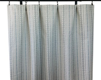 May include: A pair of light-colored curtains with a repeating pattern of vertical stripes and diamond shapes. The curtains are hung on a black rod with black rings. The fabric appears to be a woven material.