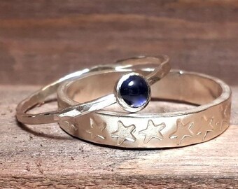 Könnte beinhalten: Zwei Silberringe mit einem blauen Edelstein, der in den oberen Ring eingefasst ist. Der untere Ring hat ein Sternenmuster.