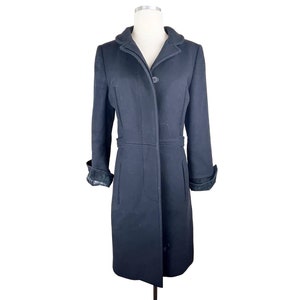 May include: A black long-sleeved coat with a single button closure and a collar. The coat has a fitted waist and a straight hemline. The sleeves have a contrasting black fabric trim.