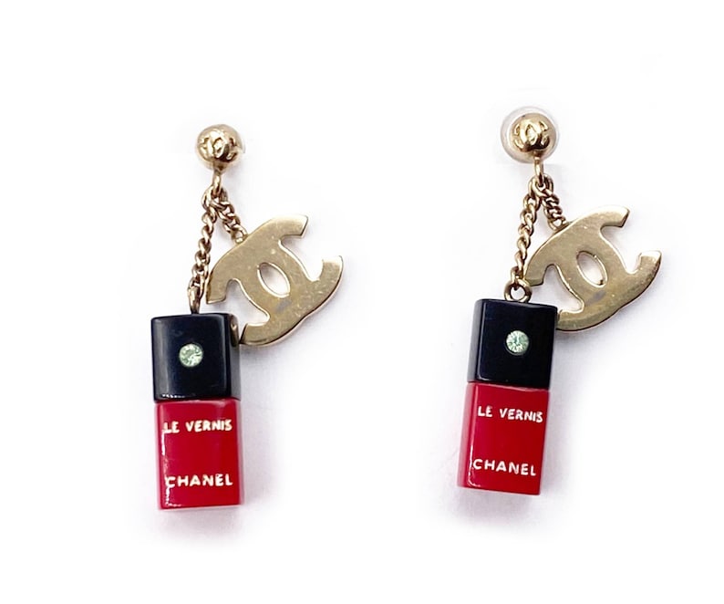 May include: A pair of gold tone earrings with a black and red nail polish bottle charm and a double 'C' logo charm. The charms hang from a gold chain.