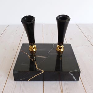 May include: A black marble pen holder with two black pen holders with gold accents. The pen holder is rectangular and features gold veining throughout the black marble.